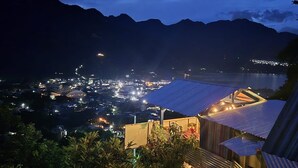 Une ville côtière de nuit, avec des bâtiments illuminés, un imposant édifice à toit bleu et une chaîne de montagnes en arrière-plan.