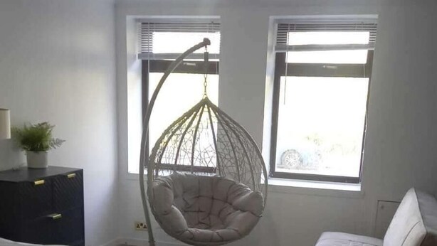 A bedroom with a bed, a hanging chair, a small sofa, and a window with blinds. - Gourock Blissful Apartment With 3 Bedrooms (Gourock)