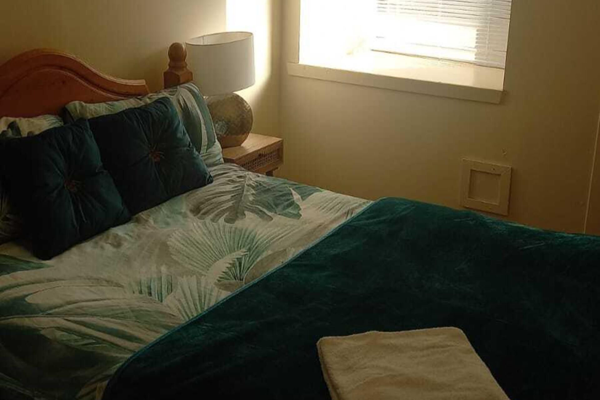 Une chambre à coucher avec un lit, une table de chevet, une lampe et une fenêtre.