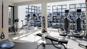 Une salle de sport moderne équipée de divers appareils d’exercice, dotée de grandes fenêtres et d’un banc.