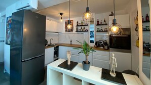 Una cocina moderna con un refrigerador negro, luces colgantes, un protector contra salpicaduras de mármol y una cafetera.