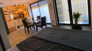 Una habitación de hotel moderna con una cama, un área de comedor con sillas y una mesa, y una cocina al fondo.