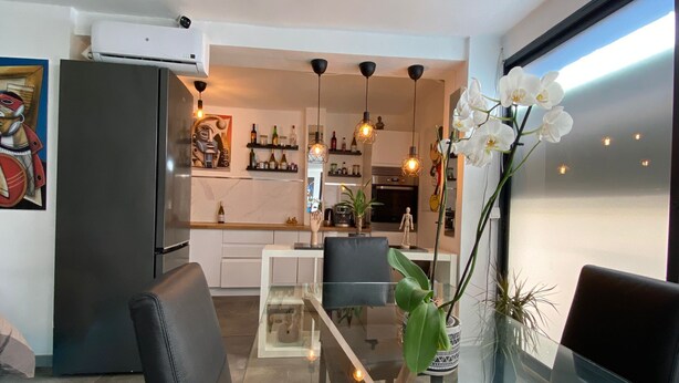 Una cocina moderna con comedor, que incluye una mesa de vidrio, sillas negras y lámparas colgantes.