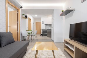 A modern living room with a sofa, a coffee table, and a TV. There is a kitchen in the background with a dining area. - Dobo Madrid América (Madrid)