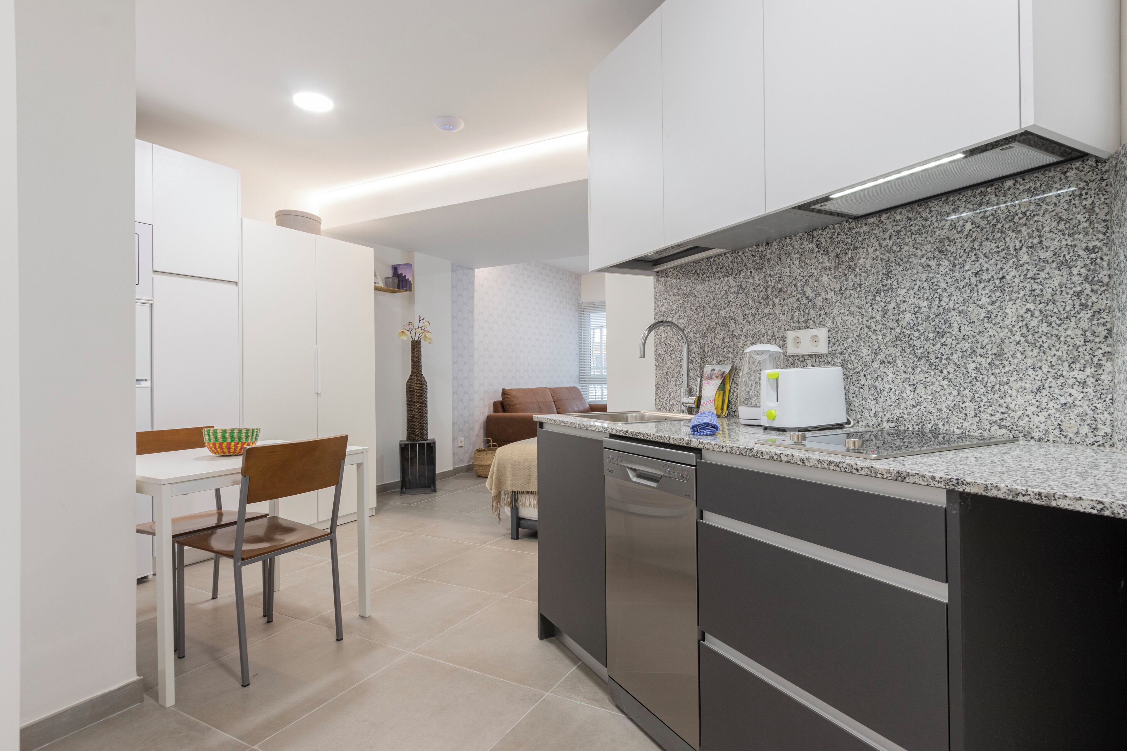Una cocina moderna con armarios blancos, encimera de granito y lavavajillas.