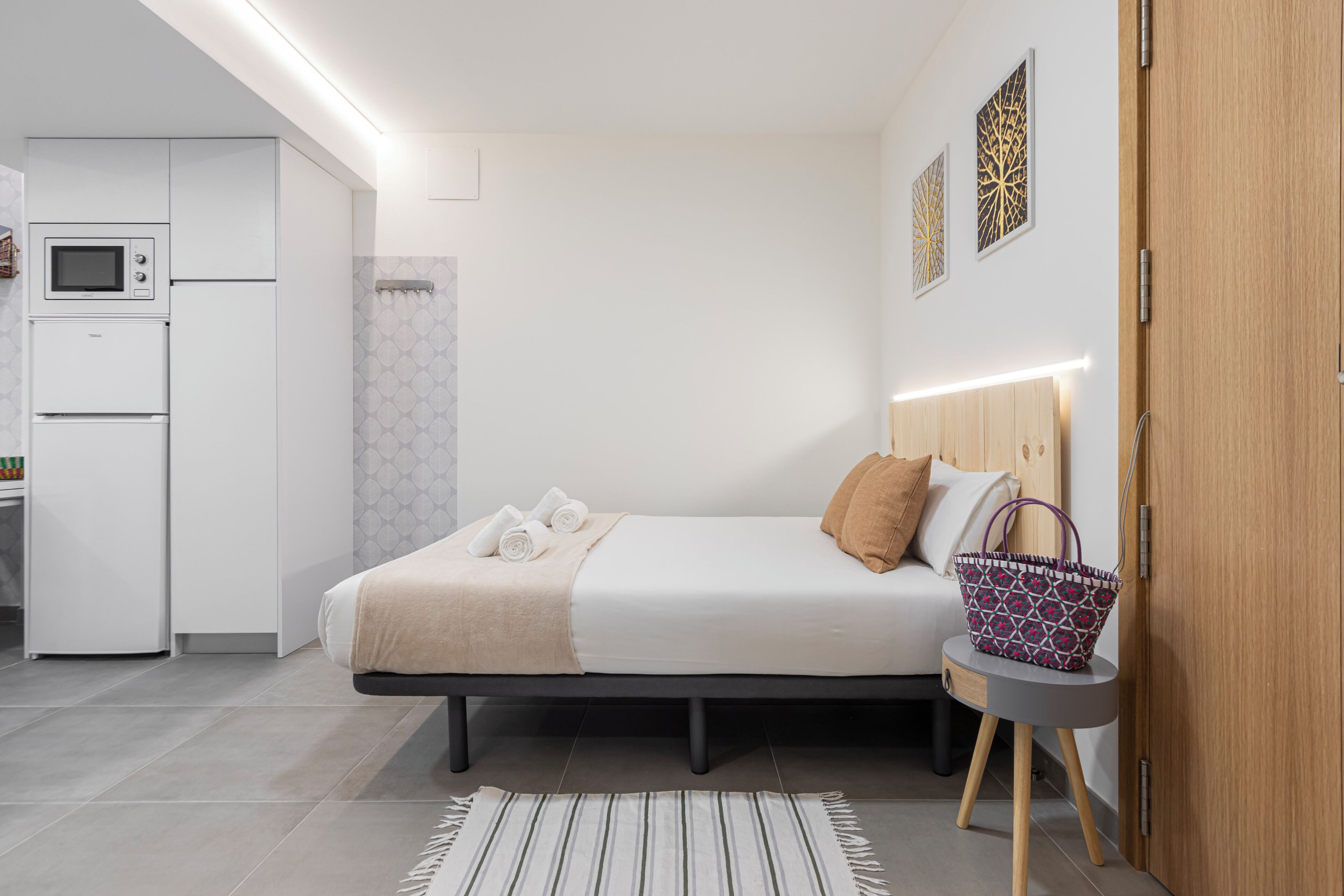 Un dormitorio moderno con cama, mesita de noche y una pequeña zona de kitchenette.