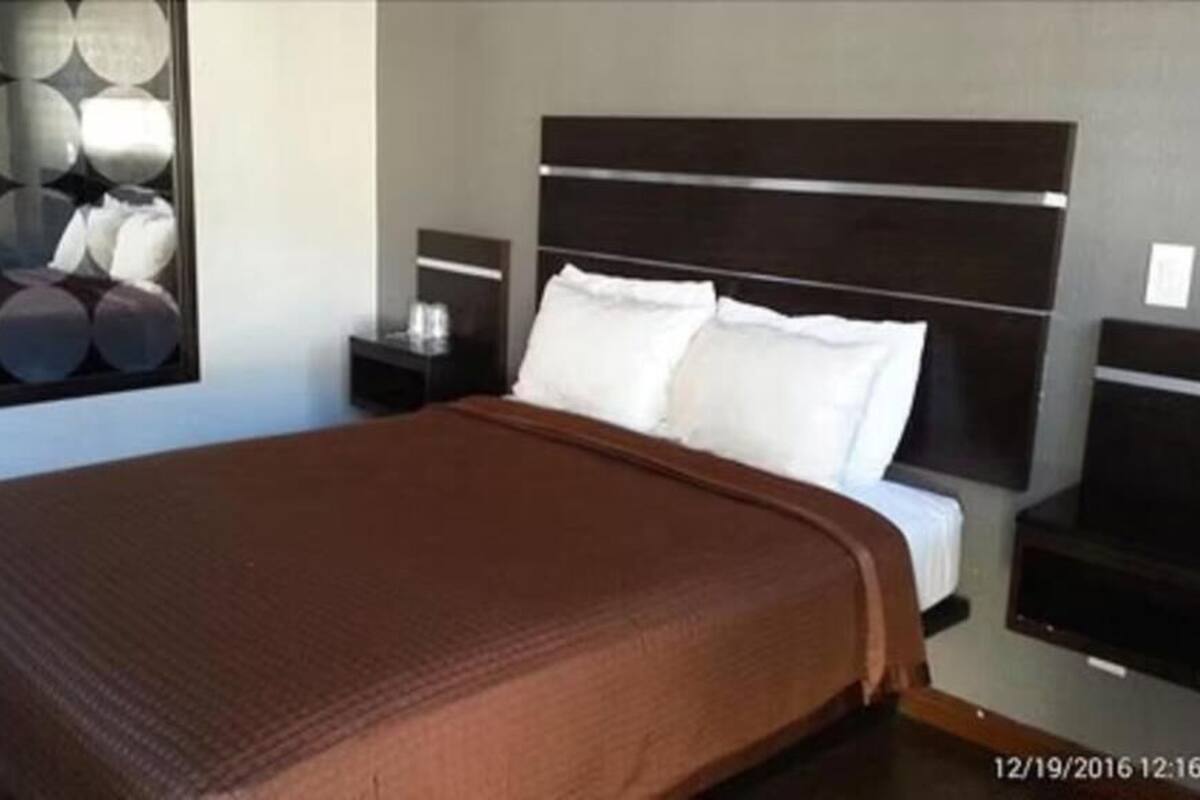 A modern hotel room with a large bed, a nightstand, a TV, and a decorative wall panel.