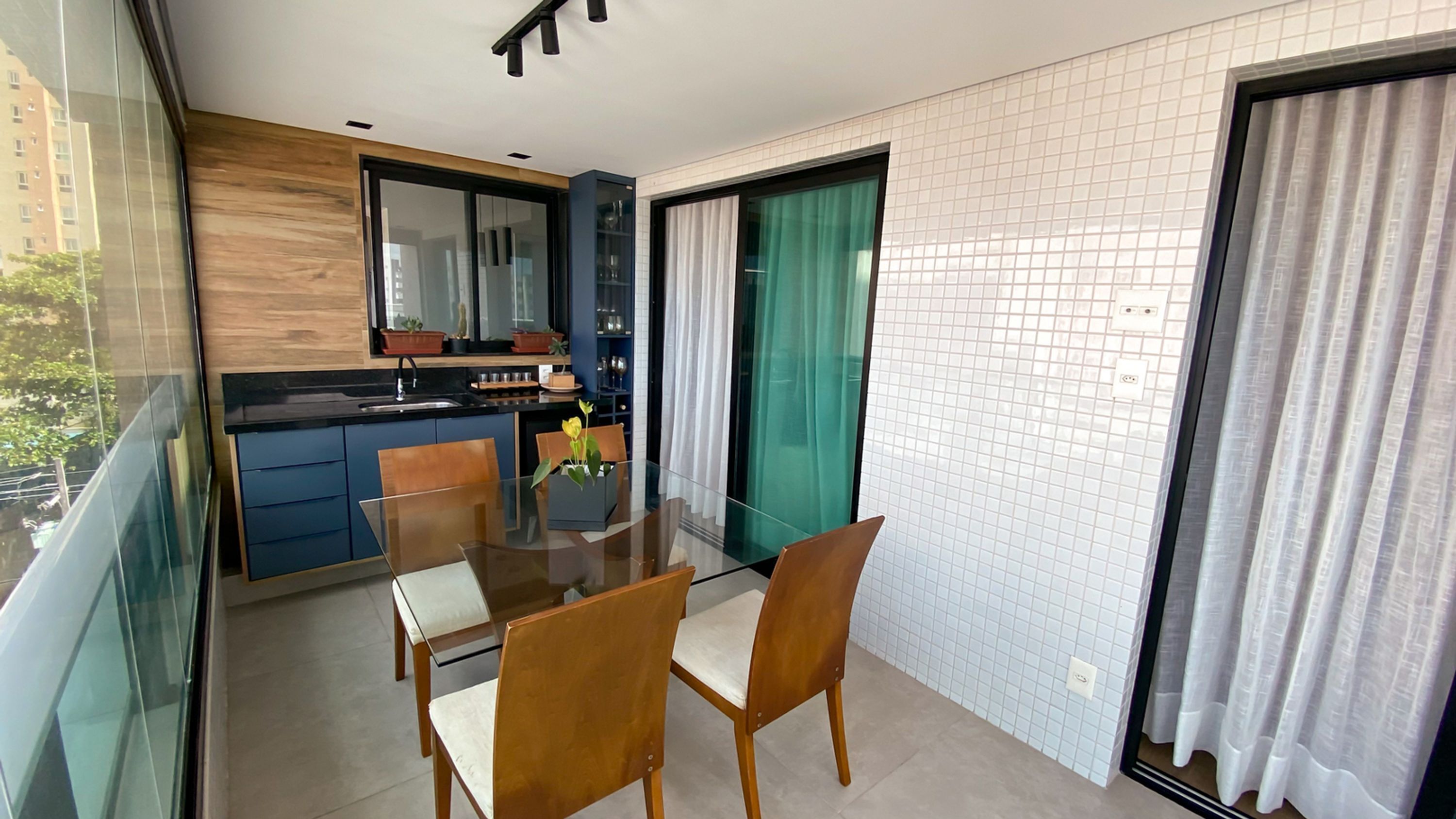 A modern kitchen with a glass dining table and chairs, a built-in oven, and a large window with curtains.
