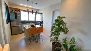 Une cuisine moderne équipée d’un réfrigérateur, d’une table à manger avec des chaises, de luminaires suspendus et d’une plante en pot.