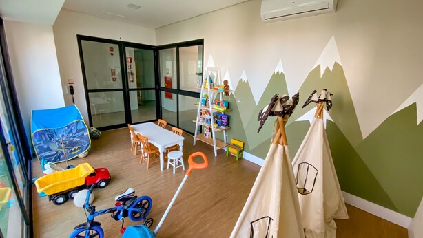 Une salle de jeux pour enfants avec une table, des chaises, des jouets et une bibliothèque.