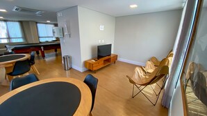 Un salon moderne avec une table de billard, un téléviseur posé sur un meuble en bois et des sièges confortables.