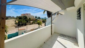 Ein Balkon mit Blick auf einen Strand, ein Gebäude und eine Palme.