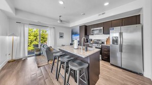 A modern kitchen with a central island, stainless steel appliances, and a large window offering a view of greenery.