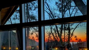 Ein Zimmer mit großen Fenstern und Blick auf Bäume sowie einen Sonnenuntergang.