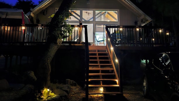 Ein zweistöckiges Haus mit einer Treppe, die zum Eingang führt, umgeben von Bäumen und einem geparkten Auto in der Nähe.