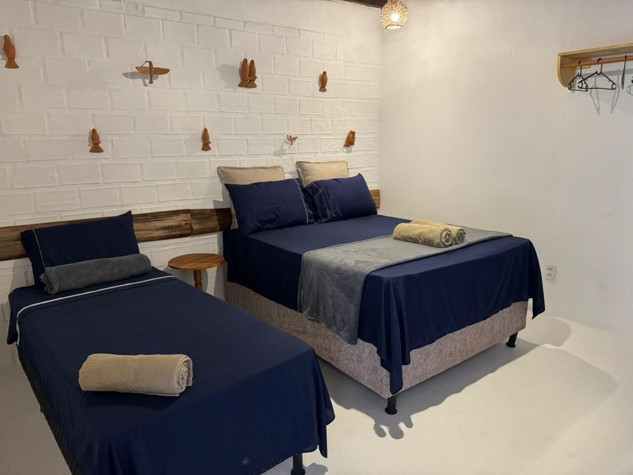 A room with two beds, each with a blue bedspread and pillows, a small round table, and a white brick wall with decorative wall mounts.