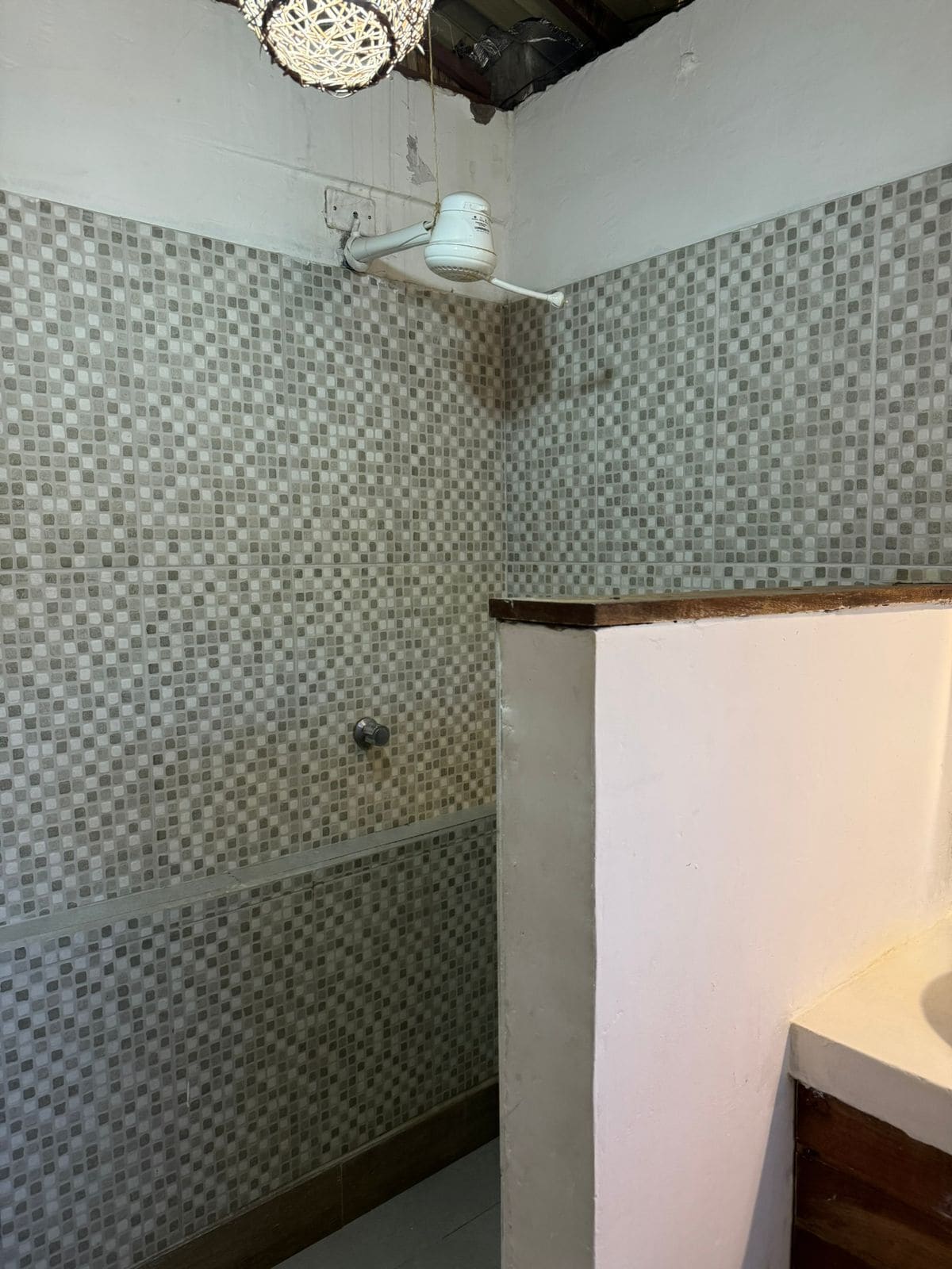 Un baño con paredes de mosaico, zona de ducha y un lavamanos blanco.