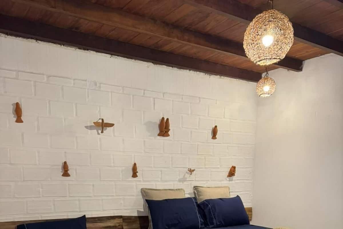 A room with two beds, white brick walls, wooden beams, and a hanging light fixture.