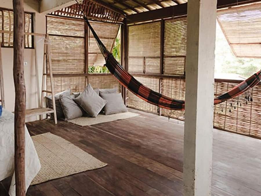 A hammock bed in a room with wooden flooring and a thatched roof.