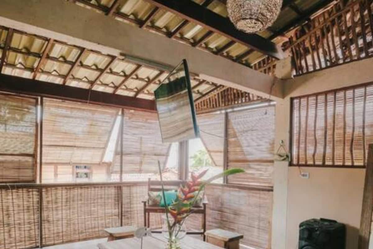 A room with a wooden table, chairs, and a woven mat. There is a large window with a view outside.