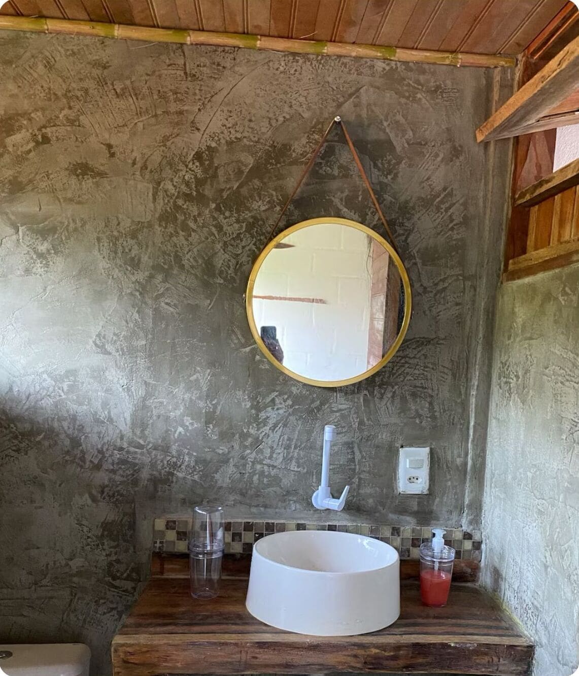 Un bagno rustico con uno specchio rotondo, un lavandino bianco e un piano d'appoggio in legno.