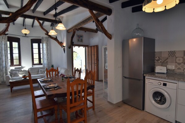 A dining area with a wooden table and chairs, a sofa, and a kitchen with a washing machine.