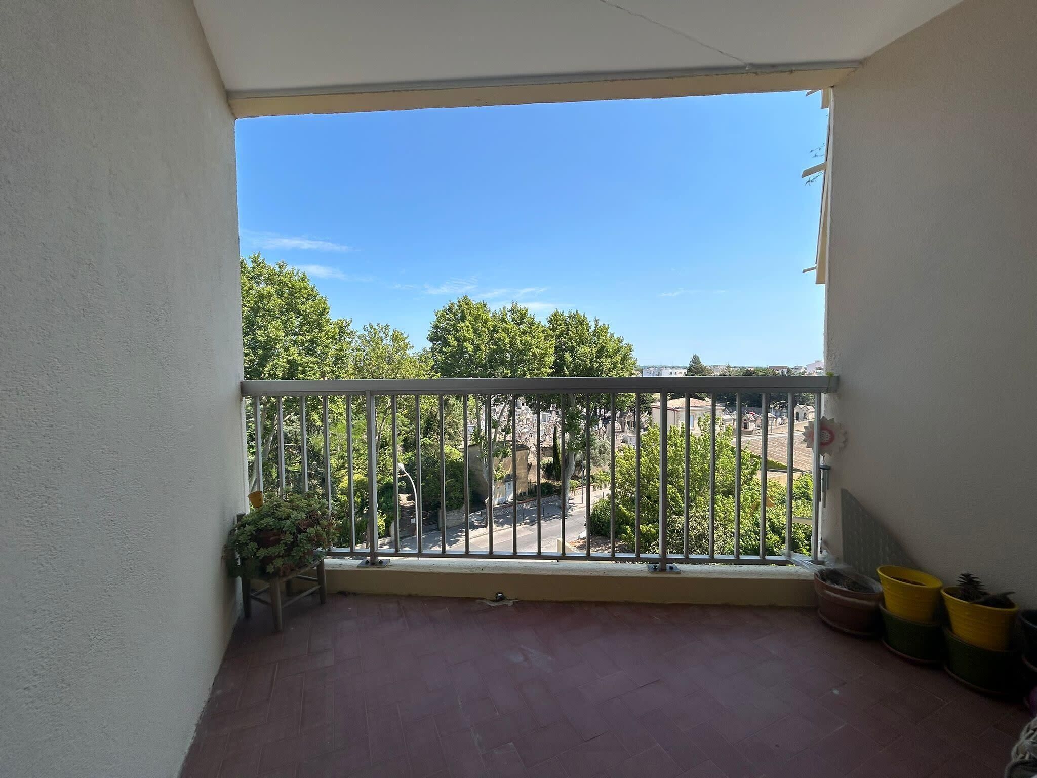 Ein Balkon mit Metallgeländer, Blumentöpfen und Blick auf eine Straße und Bäume.
