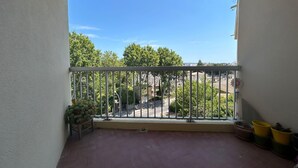 A balcony with a metal railing, potted plants, and a view of a street and trees. - Apartment with view, quiet and comfort in Narbonne (Narbonne)