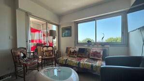 A living room with a sofa, chairs, a glass coffee table, and a large window with a view of greenery. - Apartment with view, quiet and comfort in Narbonne (Narbonne)