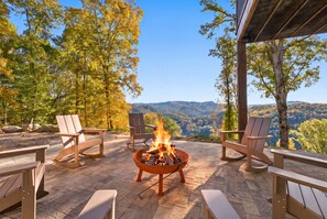 An outdoor seating area with a fire pit, chairs, and a view of the mountains.