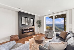 A modern living room with a fireplace, a sofa, a coffee table, and a view of the outdoors.