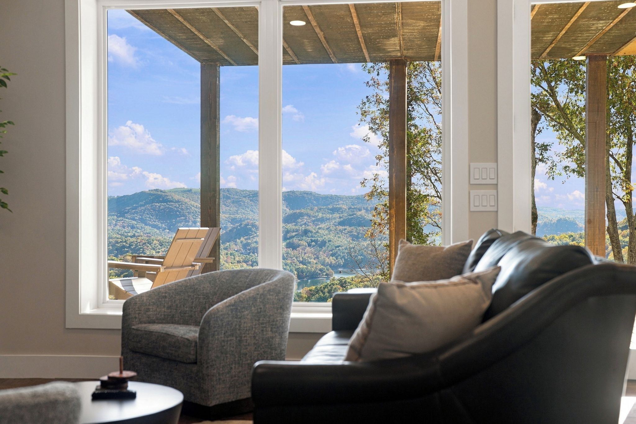 A room with a large window offering a view of a mountainous landscape. There is a sofa and a chair facing the window.