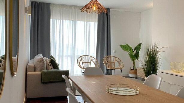En moderne stue med et træspisebord, hvide stole, en sofa og en hængende lampe.