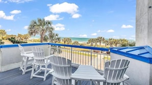 Un balcone con sedie e tavolo bianchi, affacciato su una spiaggia con palme e l'oceano.