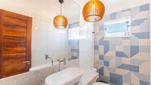 Ein modernes Badezimmer mit Holztür, einer freistehenden Badewanne, einem Waschtisch mit Spiegel und zwei Pendelleuchten.