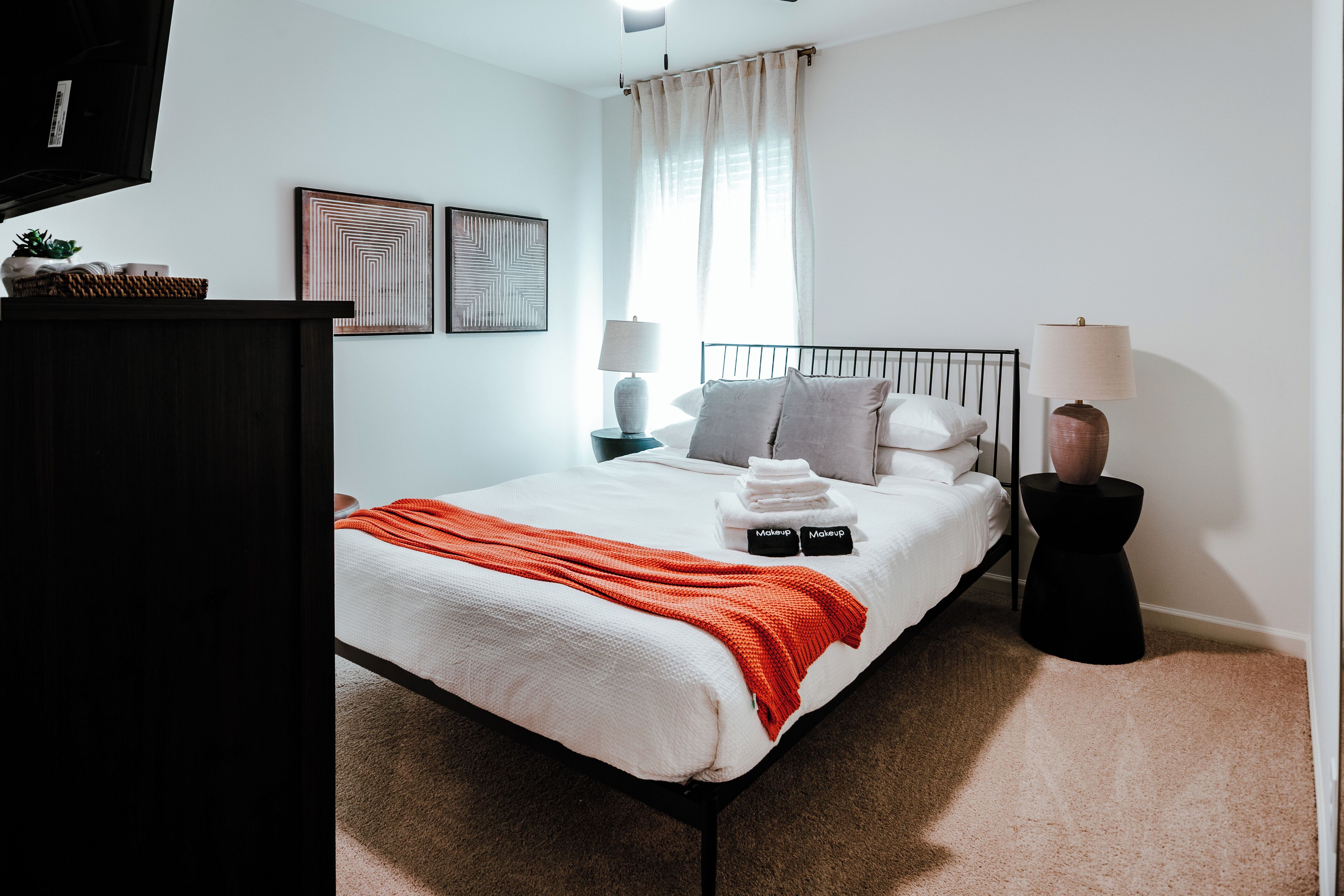 A bedroom with a bed, pillows, a bedside table, a lamp, and a wall-mounted artwork.
