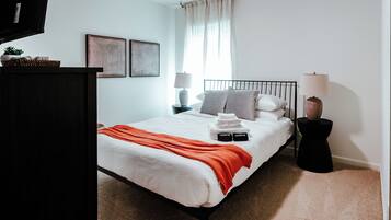 A bedroom with a bed, pillows, a bedside table, a lamp, and a wall-mounted artwork.