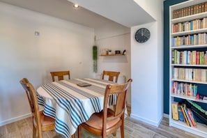 A dining area with a striped tablecloth, wooden chairs, a bookshelf with books, and a wall clock.