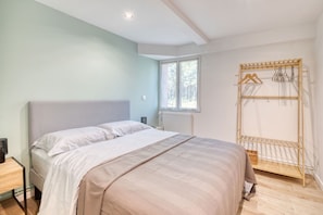 A bedroom with a bed, a bedside table, a window, and a wooden drying rack.