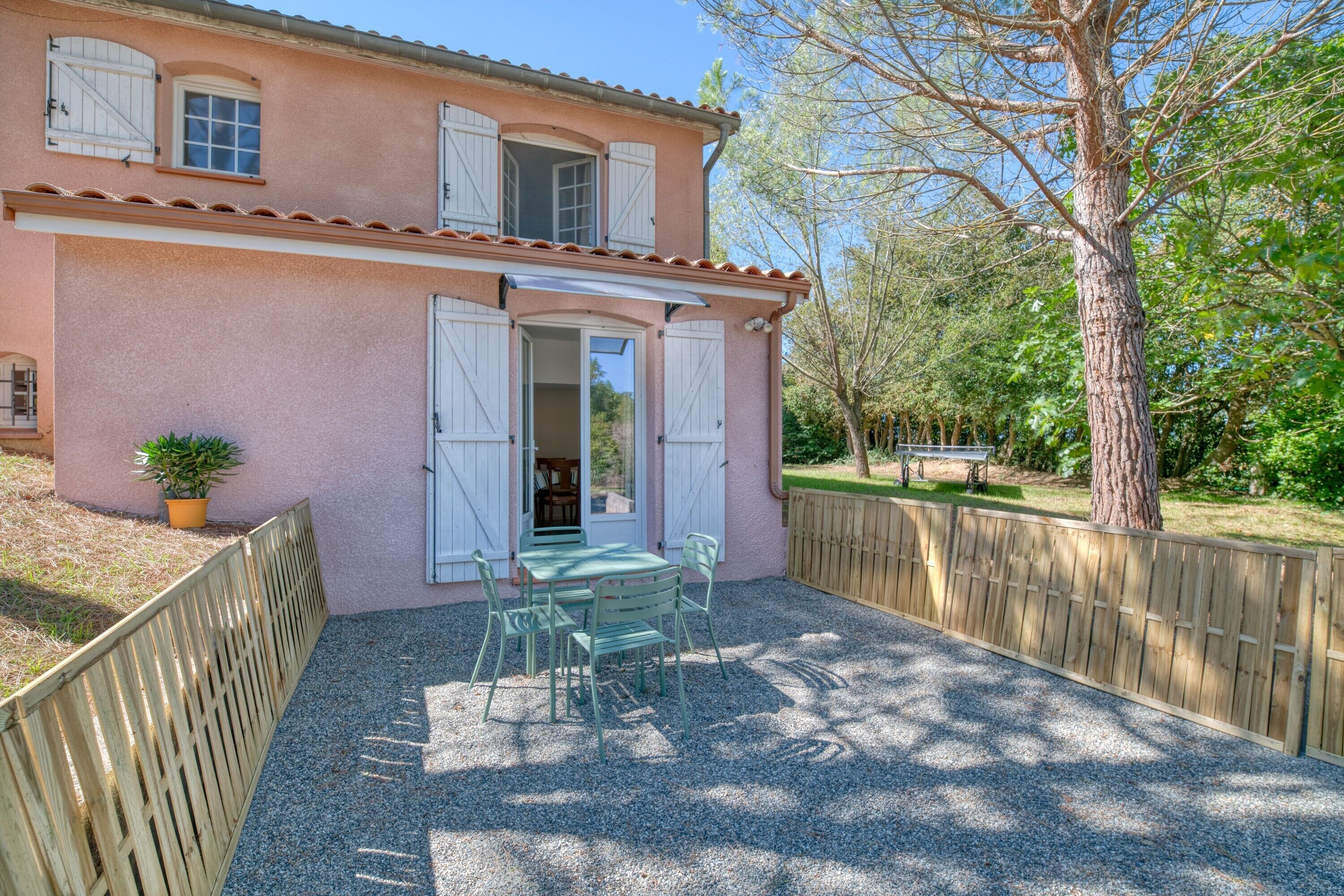 A two-story house with a patio, a table with chairs, and a wooden fence.