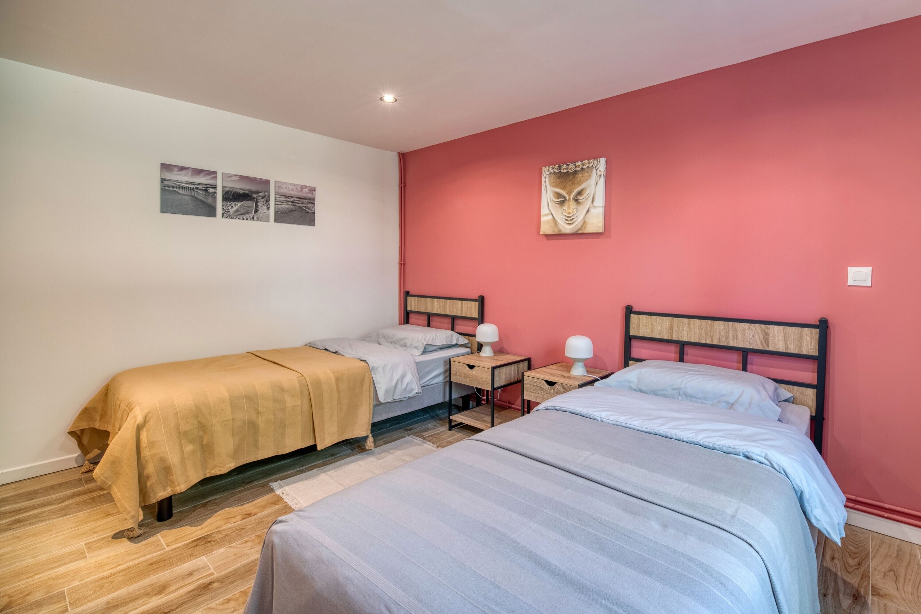 A bedroom with two beds, a red wall, and a Buddha painting.