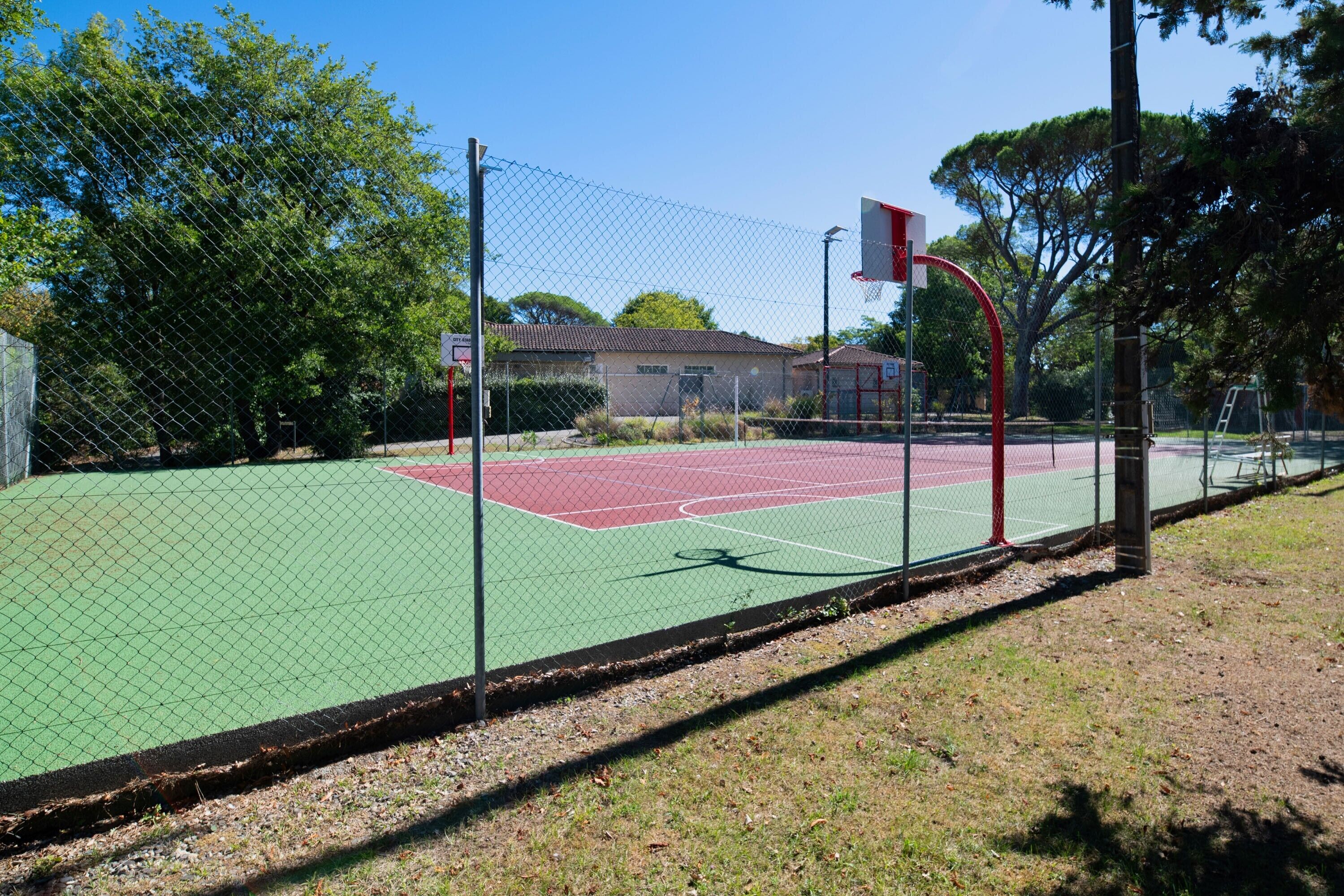 Een buitenbasketbalveld met een hek van gaas, een basketbalring en een gebouw op de achtergrond.