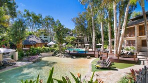Un complexe hôtelier doté d’une piscine, de chaises longues et d’un aménagement paysager de style tropical.