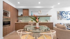 A modern kitchen with wooden cabinets, a built-in oven, and a glass dining table with chairs.
