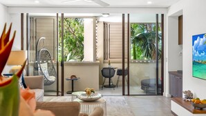 A modern living room with a glass door leading to a balcony, a hanging chair, a small table with a bottle, and a TV on the wall.