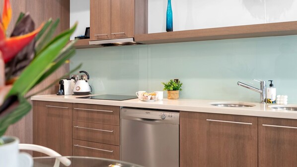 Una cocina moderna con armarios de madera, lavavajillas, hervidor y pileta.