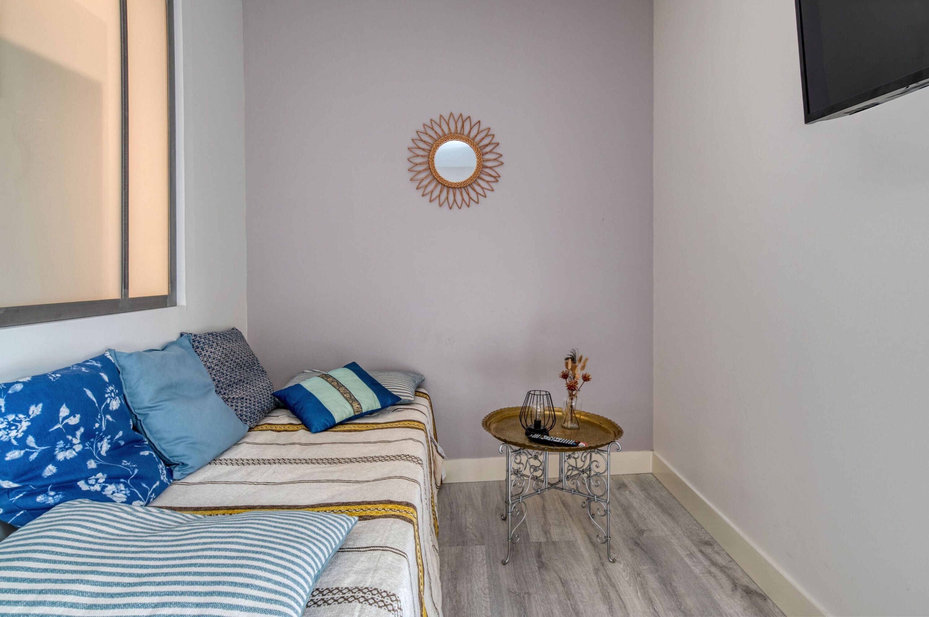 Ein Schlafzimmer mit einem Bett, einem kleinen runden Tisch mit einer Vase und einem wandmontierten Spiegel.