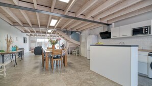 A modern kitchen with a central island, wooden beams, and a dining area with a staircase.