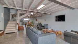 A spacious living area with a staircase, grey sofa, coffee table, and a flat-screen TV mounted on the wall.