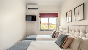 Een slaapkamer met twee bedden, een televisie en een raam met uitzicht op gebouwen.
